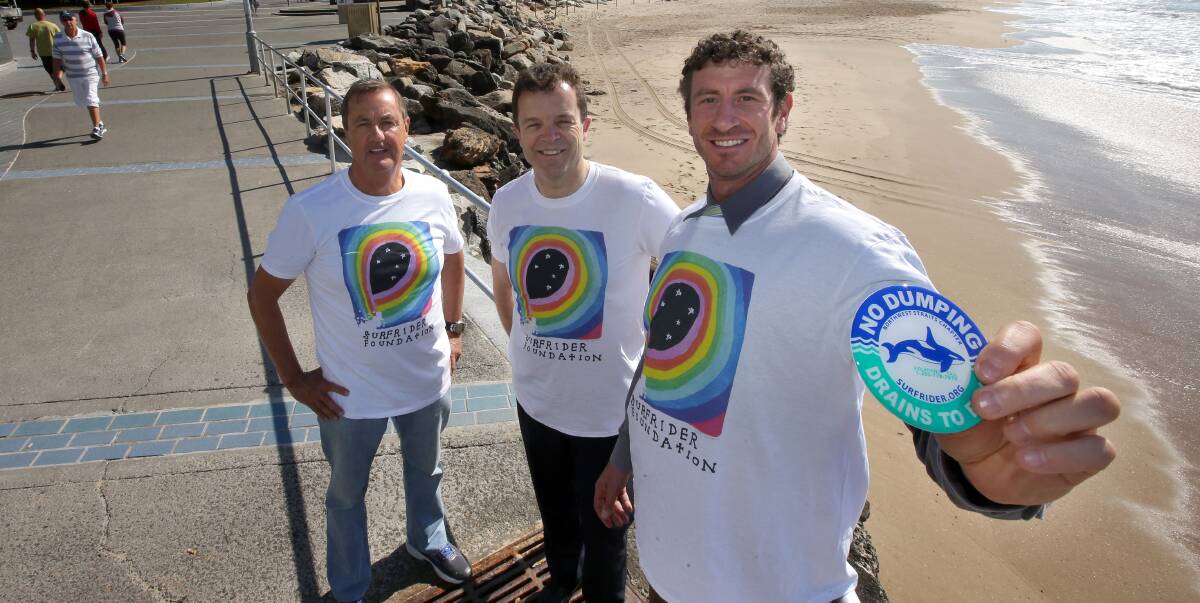 Cleaner waves: Surfrider Foundation members Mark Aprilovic and Joe Glendinning show the resin sticker with the Environment Minister Mark Speakman at the North Cronulla beach drain. Picture: John Veage
