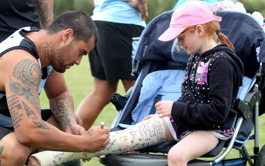On the line: Andrew Fifita helped out young Tahli Cooper by signing the cast of the leg she broke which prevented her taking part in Tuesday's Sharks Junior Jaws holiday clinic for school children. Now Sharks fans are hoping Fifita signs a new contract to stay at Woolooware. Picture: Chris Lane