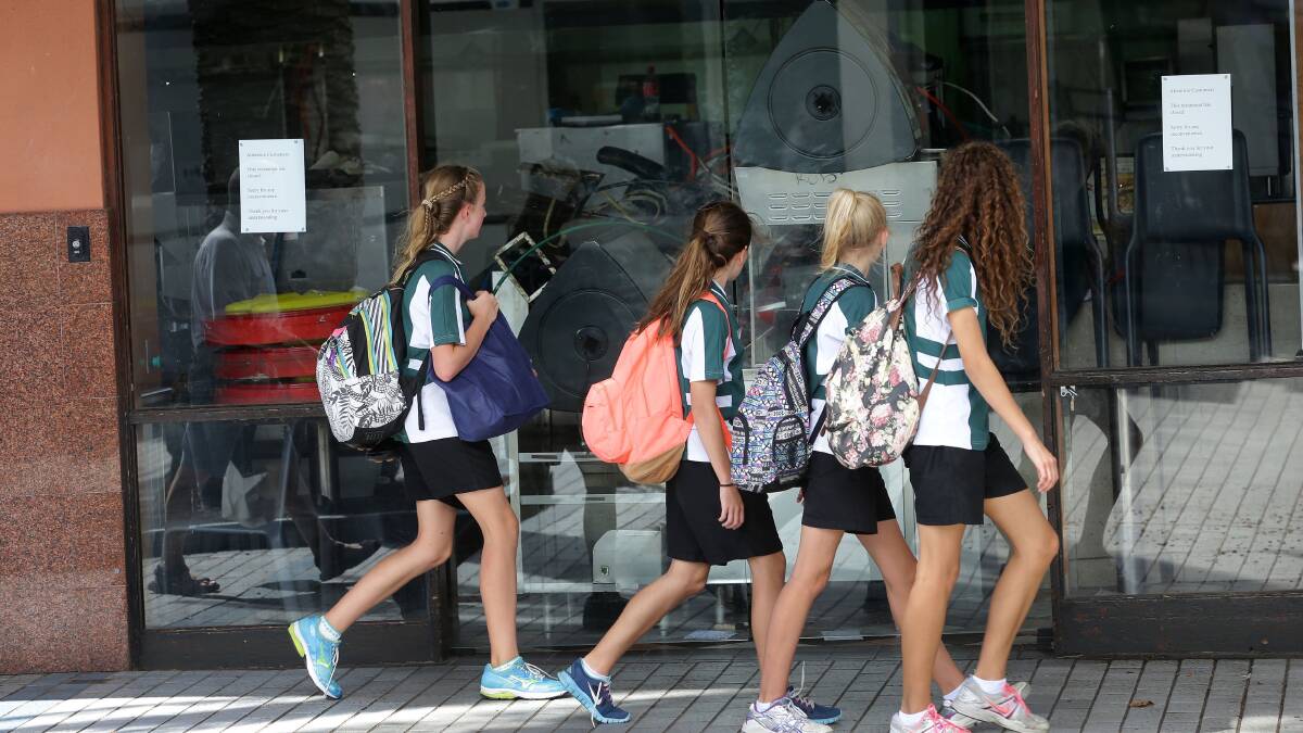 Still wondering: Students walk past the Cronulla McDonald's site. The handwritten notes about its closure have been replaced with typed ones. Picture: John Veage.

