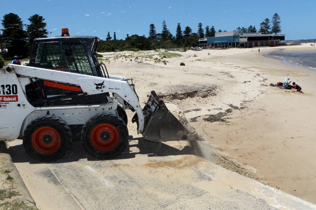 Never-ending job: A council contractor returns sand to the beach after it was blown onto paths by the wind. Picture: Lisa McMahon