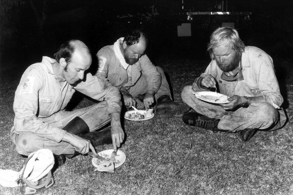 Remembering: Grays Point bush fire firemen (from left) Brian Bennett, Peter Junhans and Paul Ripley from the Sandy Point Bushfire Brigade, eat their dinner on the front lawn of a house in Angle Street, Grays Point, during a break in the firefighting on January 9, 1983. SMH Picture by Peter Solness