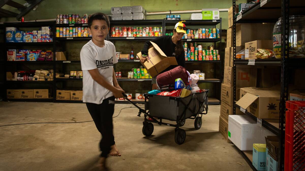 Macen Hickling, 9, picks up some supplies from the Koori Kitchen's food bank in Lismore while Maighan Lawson unpacks donated goods in the background. 
