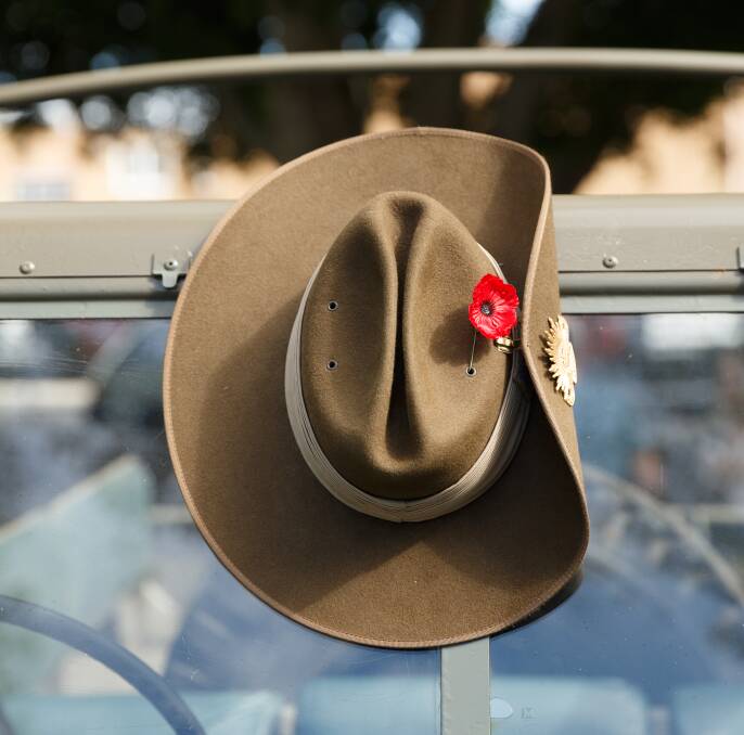 A slouch hat adorned with red poppy hangs from a Land Rover in an Anzac Day procession. Picture: Max Mason-Hubers