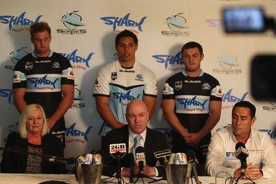 All smiles: Cronulla chairman Damian Irvine (middle) with SHARK Energy’s Fiona Kay and coach Shane Flanagan with players showing the new-look Cronulla jersey. Picture: John Veage